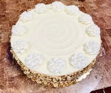 Carrot cake with cream cheese frosting and chopped nuts around the base