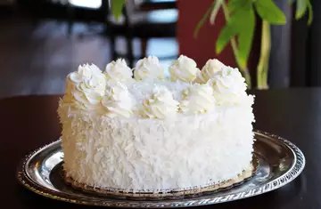 Coconut cream cake covered in shredded coconut with piped cream rosettes