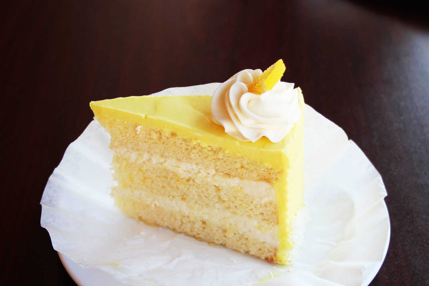 A slice of lemon dream cake showing its layers, topped with cream and candied lemon