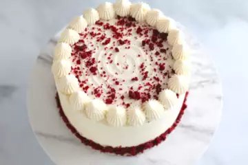 Red velvet cake in white frosting, edged with piped rosettes and red velvet crumb