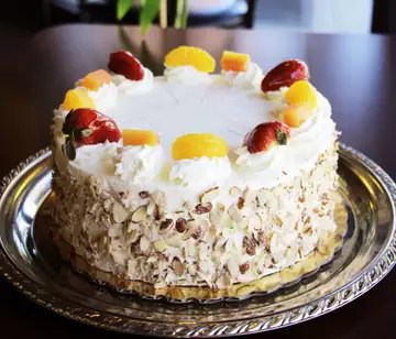 White chocolate fruit cake edged in sliced almonds and topped with fresh fruit